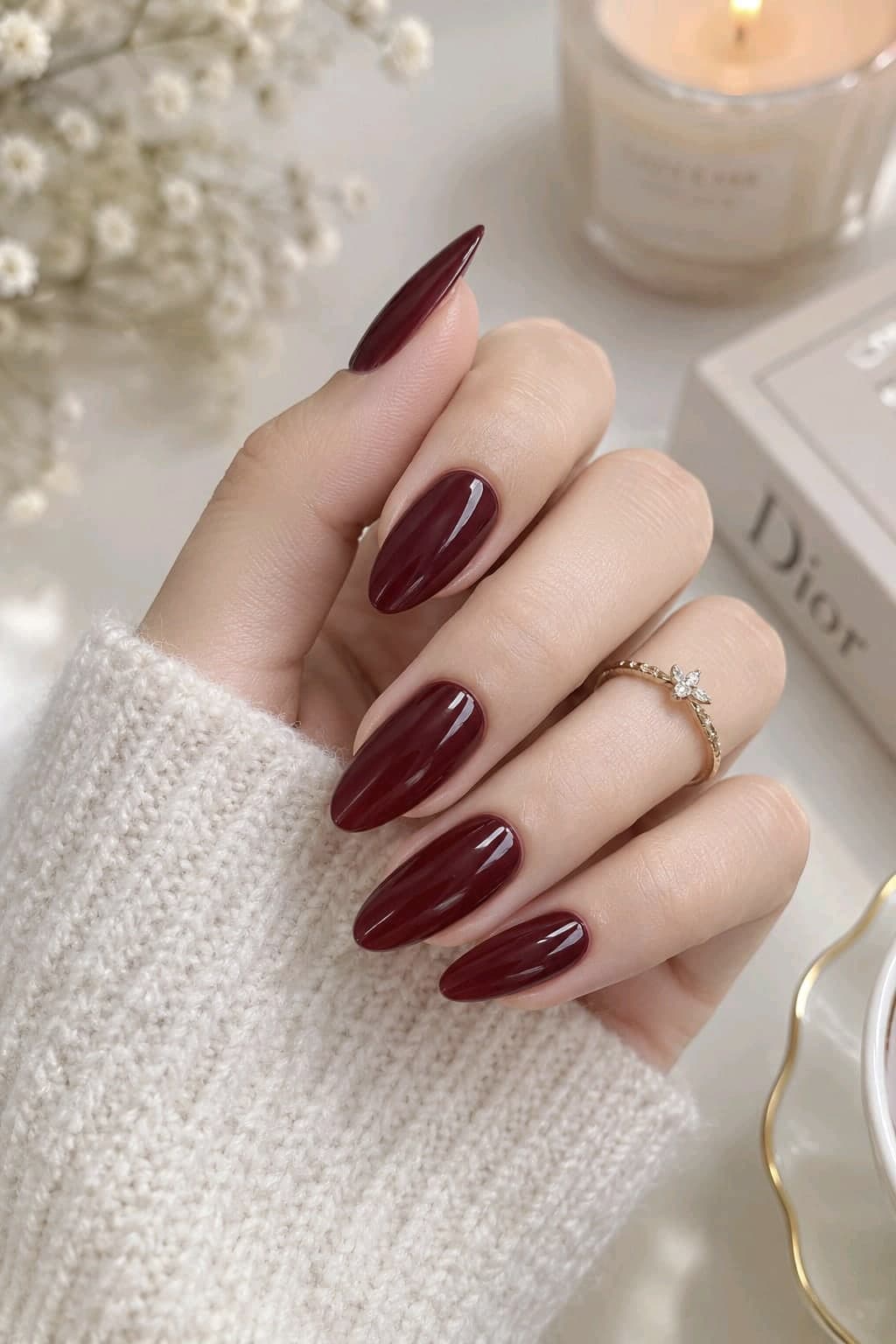 Glossy burgundy wine red almond nails with a dainty gold flower ring