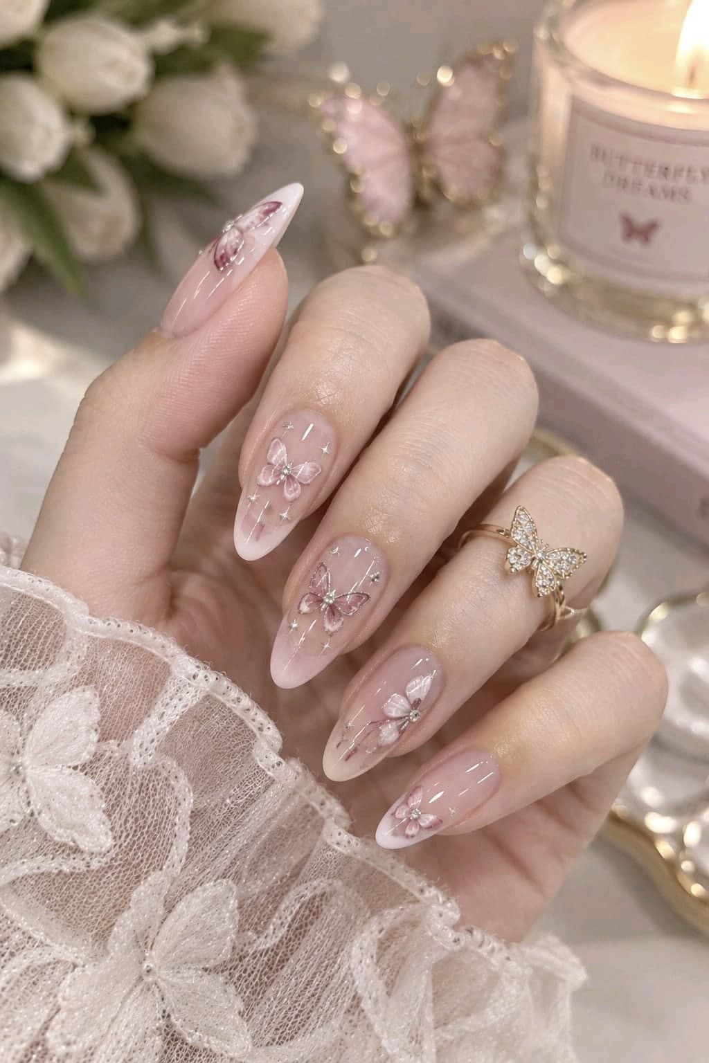 Soft pink almond nails with pink butterflies, white ombré tips, tiny stars and a gold butterfly ring