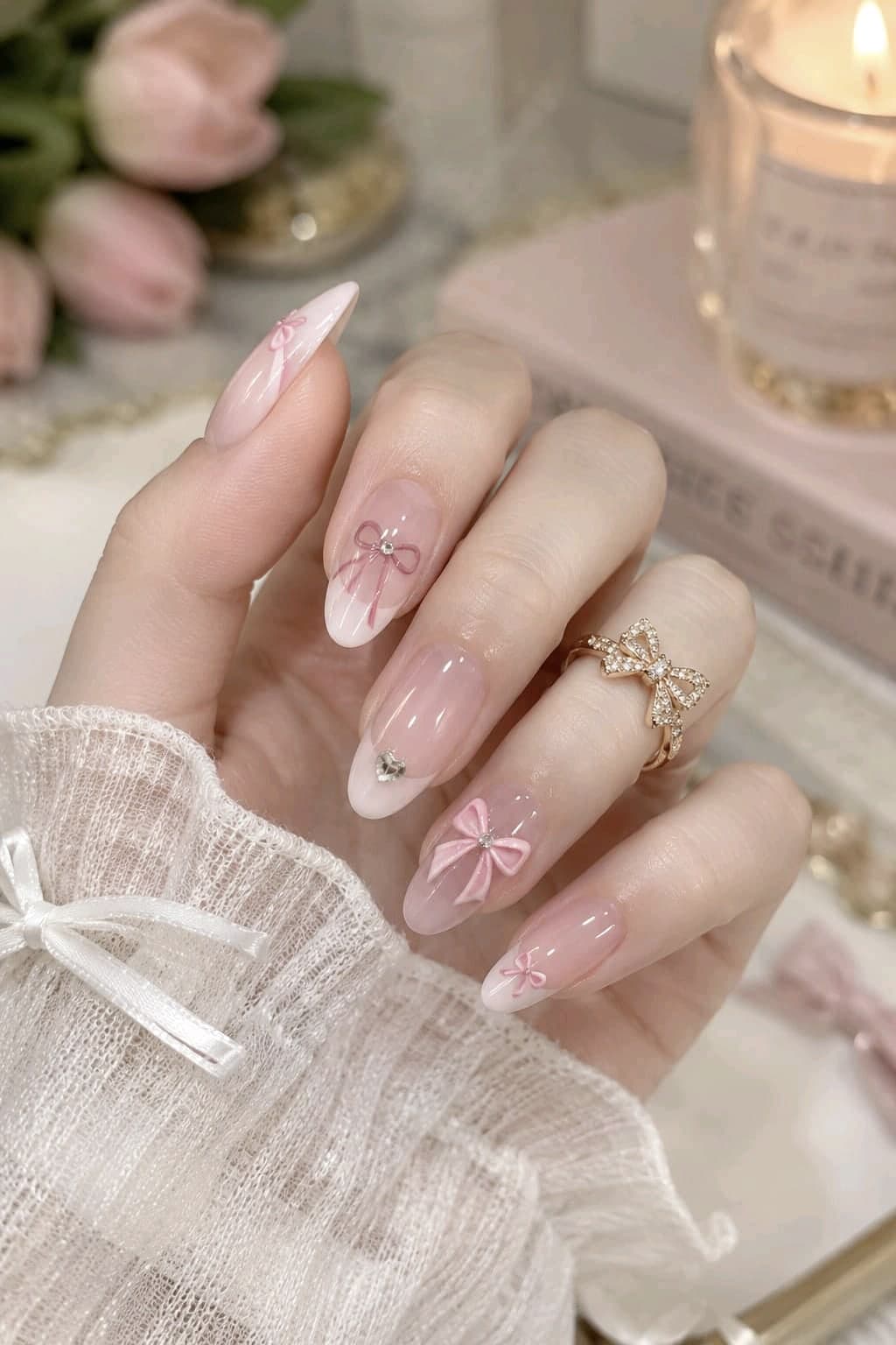 Soft pink ombré almond nails with painted pink bows, a 3D pink bow, a heart gem and a gold bow ring