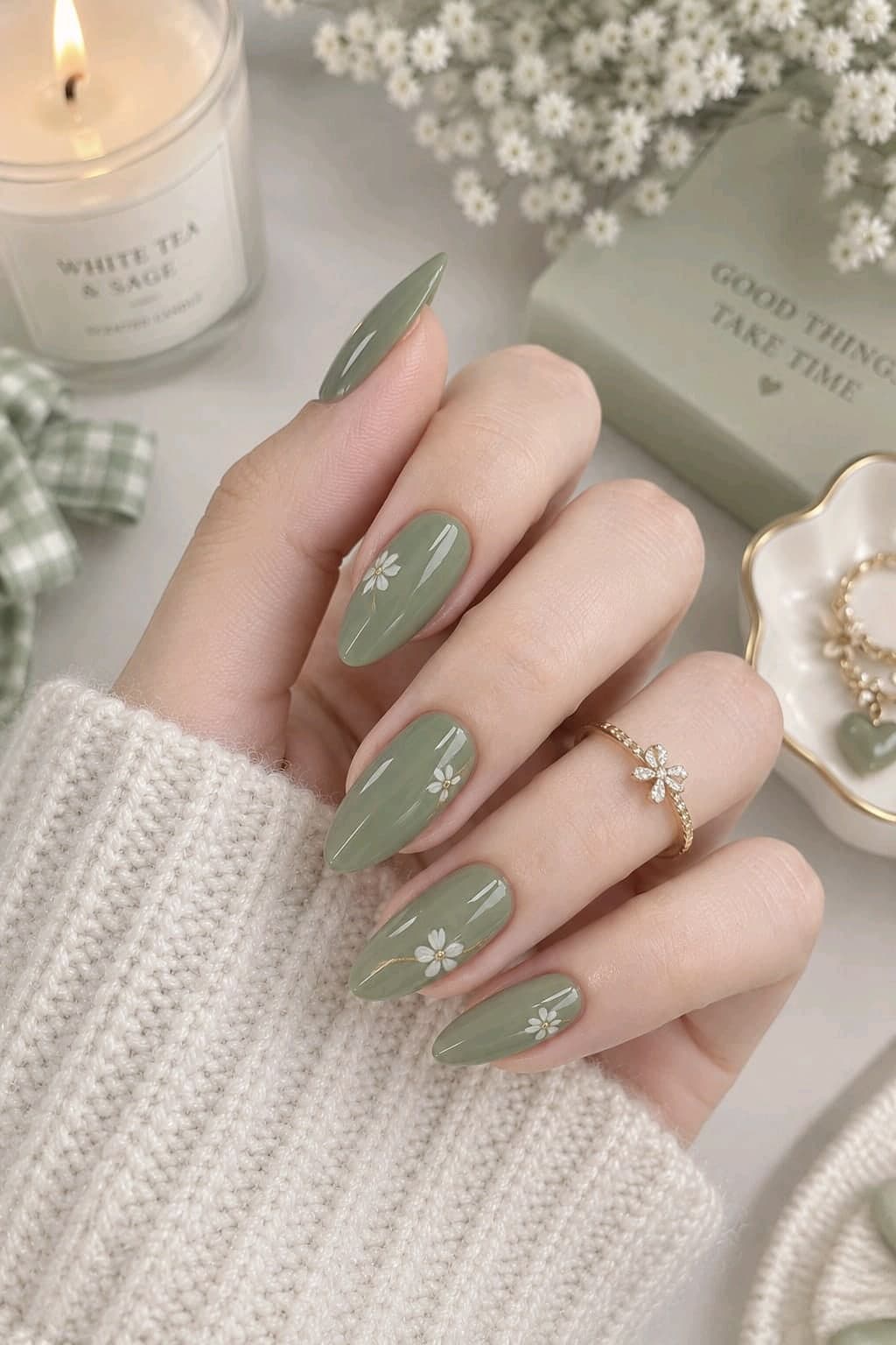 Sage green almond nails with small hand-painted white flowers and a gold flower ring