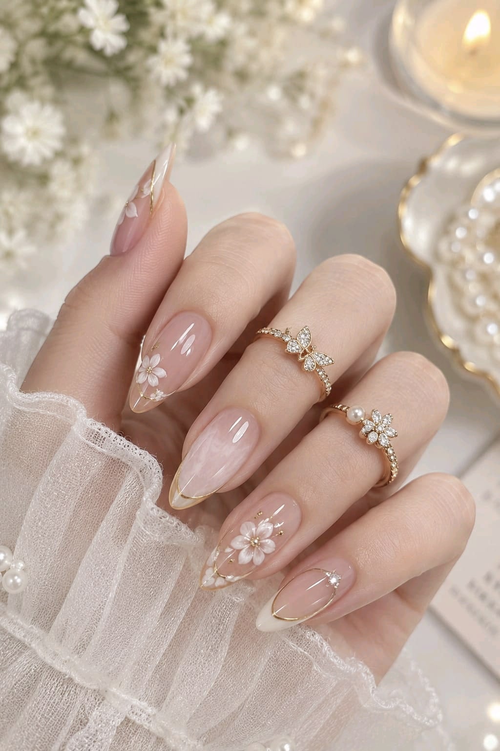 Long almond nails with nude base, white floral art and thin gold French tip outlines