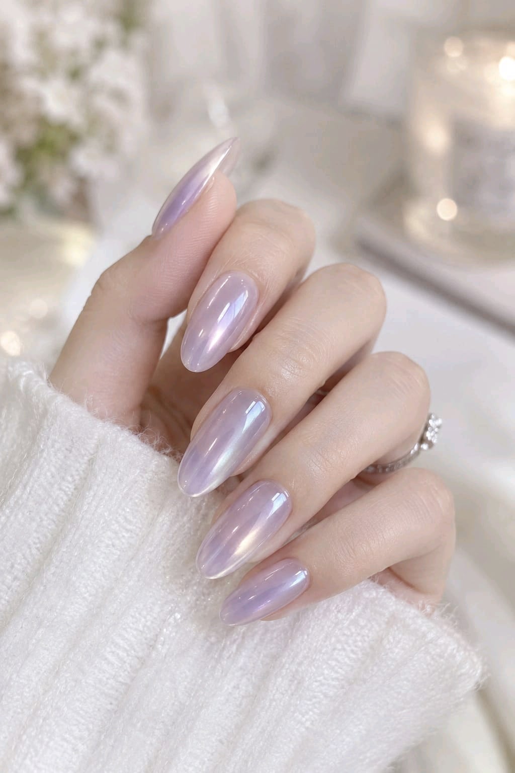 Long almond nails with an iridescent lilac pearl chrome finish and a white knit sweater
