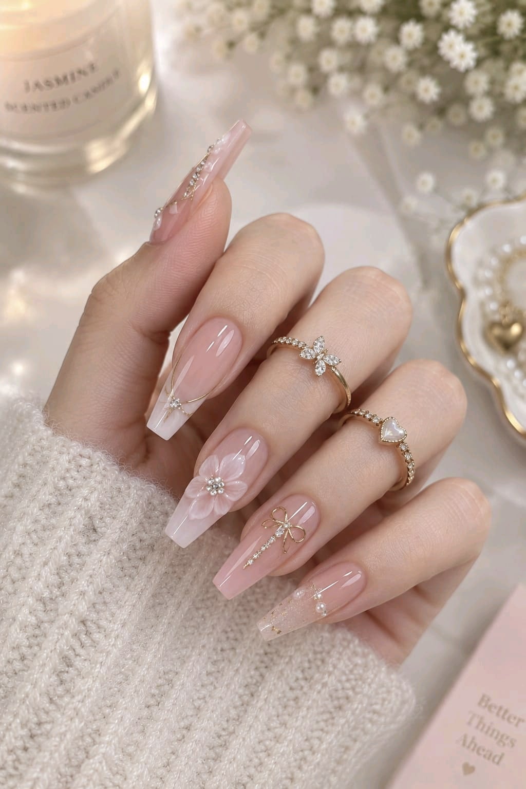 Long soft pink coffin nails with a 3D white flower, gold bow charm, pearls and gold French lines